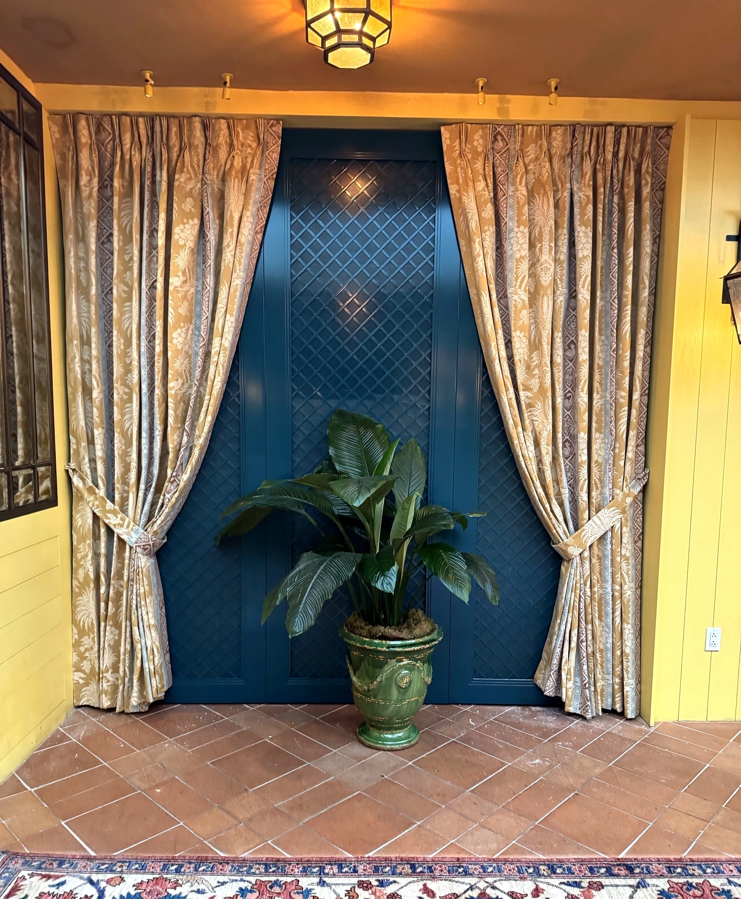 Custom pinch pleat drapery with fabric tie backs framing a teal lacquered doorway at The Conservatory, Fifth Avenue Hotel, New York